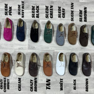 K&ouml;nnte beinhalten: Eine Auswahl an Wildleder- und Lederschuhen in verschiedenen Farben, darunter Marineblau, Pink, Schwarz, Gr&uuml;n, Grau, Beige, Braun und Orange. Die Schuhe sind auf einer hellgrauen Oberfl&auml;che mit Farbbezeichnungen angeordnet.