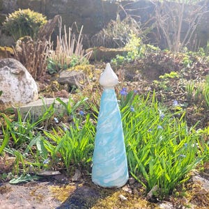 Könnte beinhalten: Eine Keramik-Gartenskulptur in Form eines hohen, schlanken Kegels. Die Skulptur ist in Blautönen und Weiß bemalt, mit einem wirbelnden Muster. Die Spitze der Skulptur ist abgerundet und weiß.