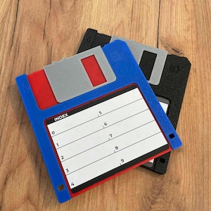 以下が含まれることがあります： 木製の表面に、青と黒のフロッピーディスクが2つあります。青いフロッピーディスクには、"INDEX"という単語と数字が書かれた白いラベルが付いています。