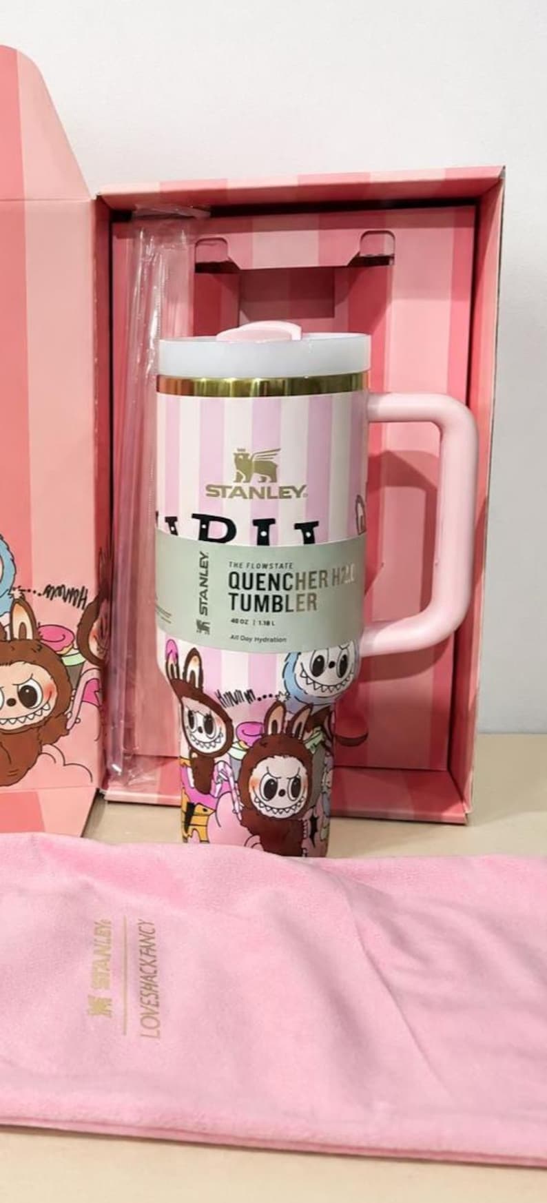May include: A pink Stanley Quencher H2.0 tumbler with a white lid and handle, presented in a matching box. The tumbler features a striped design and cartoon graphics. The capacity is 40 oz.