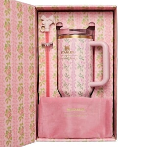 May include: A pink Stanley mug with a floral pattern, presented in a matching gift box. The mug has a handle and a lid, and includes a pink straw and a pink velvet pouch. The box and mug feature the "Stanley" logo.
