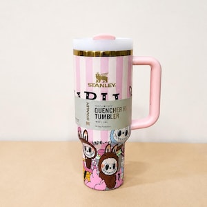 May include: A pink and white striped Stanley Quencher H2.0 Flowstate tumbler with a pink handle and lid. The tumbler features a colorful cartoon design and holds 40 oz (1.18L) of liquid.