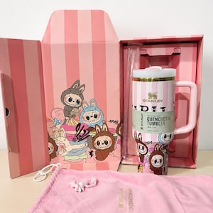 May include: A pink Stanley Quencher H2.0 FlowState tumbler with a white lid and handle, inside a matching pink box with a cartoon bunny design. Includes a pink drawstring bag and a small bunny-shaped charm.
