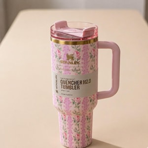 May include: A pink floral Stanley Quencher H2.0 tumbler with a handle and lid. The tumbler features a pink and white floral pattern, a gold band, and the text "LOVESHACKFANCY". It holds 40 oz.