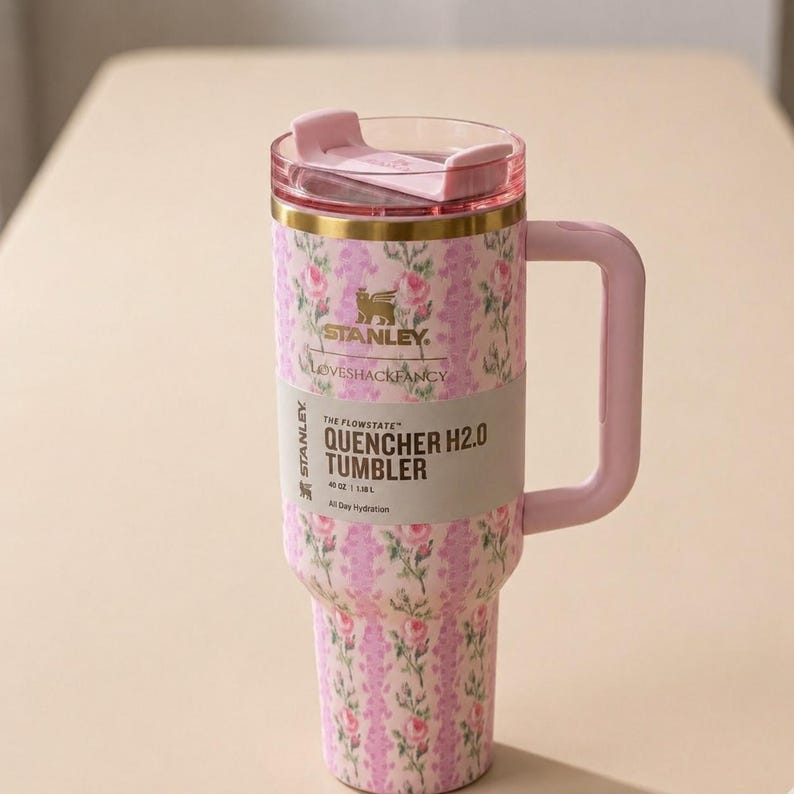 May include: A pink floral Stanley Quencher H2.0 tumbler with a handle and lid. The tumbler features a pink and white floral pattern, a gold band, and the text "LOVESHACKFANCY". It holds 40 oz.