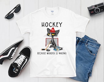 Op de afbeelding: Wit T-shirt met een zwarte kat die een rood-witte hoed draagt, een hockeystick vasthoudt en voor een hockeydoel staat. De tekst "Hockey because murder is wrong" staat op het T-shirt gedrukt.