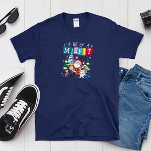 May include: Navy blue t-shirt with the text "A bit of a Misfit" in colorful letters. The shirt features a graphic of Santa Claus and other characters. Black and white sneakers, sunglasses, and a camera are also in the image.