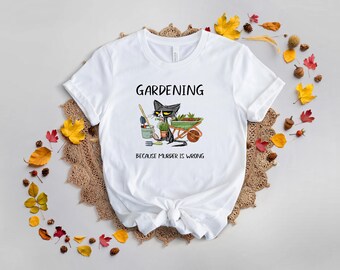May include: White t-shirt with a black and white cartoon cat gardening. The text on the shirt reads "Gardening because murder is wrong."