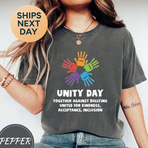 May include: Dark gray t-shirt with a colorful handprint design and the words "UNITY DAY" above the text "TOGETHER AGAINST BULLYING UNITED FOR KINDNESS, ACCEPTANCE, INCLUSION". The shirt also has the text "SHIPS NEXT DAY" and "PEPPER".