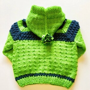 May include: A green knitted hooded sweater with blue stripes and a pom-pom on the hood.