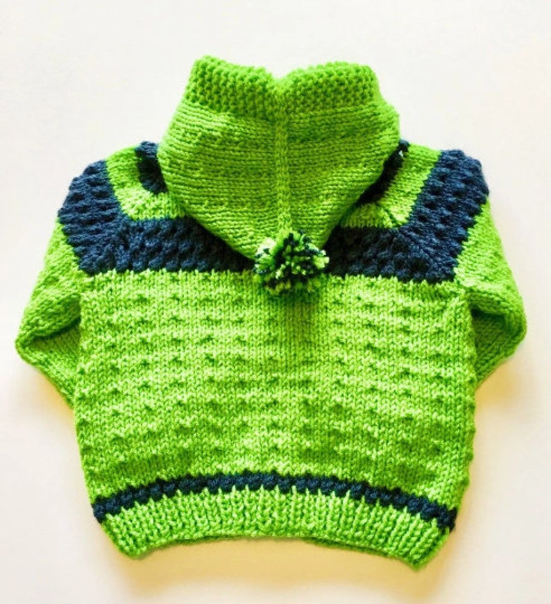 May include: A green knitted hooded sweater with blue stripes and a pom-pom on the hood.