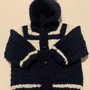 May include: A navy blue knitted baby cardigan with white stripes and a matching hood with a white pom pom.