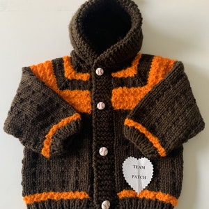 May include: A brown and orange knitted hooded cardigan with baseball buttons and a white heart-shaped tag that says "Team Patch".