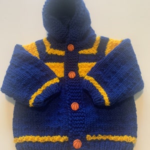May include: A blue and yellow knitted hooded cardigan with basketball buttons. The cardigan has yellow stripes on the sleeves and bottom.