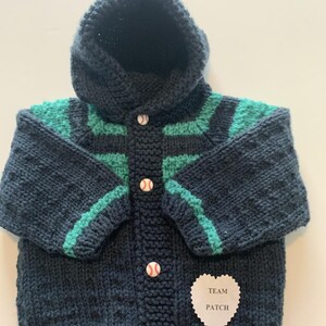 May include: A dark blue knitted hooded jacket with green stripes and baseball buttons. The jacket has a heart-shaped patch that says "Team Patch".