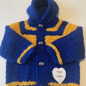 May include: A blue and gold knitted hooded jacket with football-shaped buttons. The jacket has gold stripes and a pom-pom on the hood. A white heart-shaped patch with the words "TEAM PATCH" is sewn on the front.