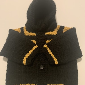 May include: Black knitted baby cardigan with yellow stripes and a hood with a pom pom on top.