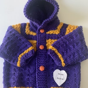 May include: Purple and gold knitted baby cardigan with a hood and basketball buttons. The cardigan has a heart-shaped tag that says "Team Patch".