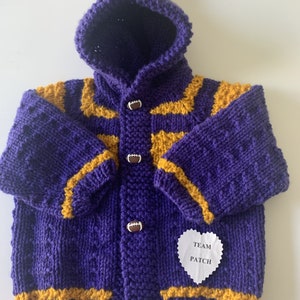 May include: Purple and gold knitted baby cardigan with a hood and football buttons. The cardigan has a heart-shaped patch that says "Team Patch".