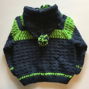 May include: A dark blue knitted hooded sweater with green trim and a green pom-pom on the hood.