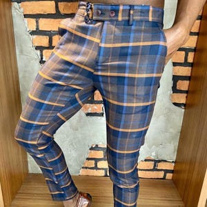 Pode incluir: Calças xadrez de corte justo em tons de azul, castanho e laranja. As calças apresentam um padrão xadrez clássico e são combinadas com mocassins de couro castanho. As calças têm um corte sob medida.