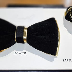 May include: Black velvet bow tie with gold trim and a matching black and gold flower lapel pin. The text "BOW TIE" and "LAPEL PIN" are printed on the white card.