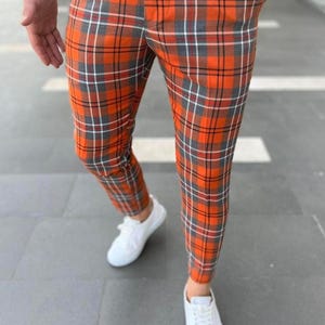 May include: Orange and gray plaid pants with a classic check pattern. The pants are paired with white sneakers. The trousers have a tailored fit and are made of a woven fabric.