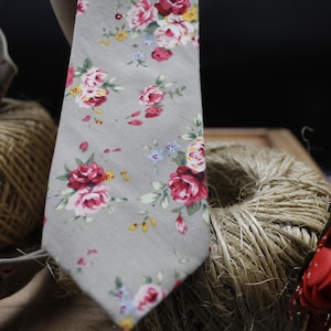 May include: A grey floral patterned tie with pink, red and yellow flowers. The tie is made of a soft, cotton fabric.