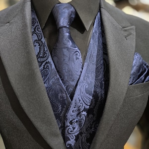 May include: A dark grey suit with a black shirt, navy blue paisley waistcoat, tie, and pocket square. The waistcoat and accessories have a detailed, swirling pattern. The suit is displayed on a mannequin.