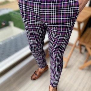 May include: Purple plaid trousers with white and black lines. The trousers are worn with brown leather loafers. The person is standing on a wooden deck. The trousers have pockets and a button closure.