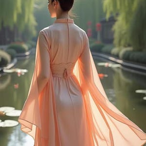 May include: A peach-colored dress with long, flowing sleeves and a high neckline. The dress features a fitted bodice with a lace detail at the waist and a flowing skirt. The model is standing near a body of water.