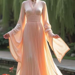 May include: A peach-colored, flowing dress with long, wide sleeves and a pleated skirt. The dress features a V-neckline and a detailed waist. The model is standing near a pond with koi fish, with a blurred green background.