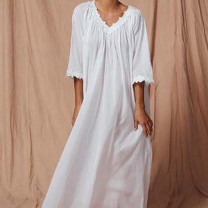 以下が含まれることがあります： Vネックとフリル付きのトリムが特徴の白い長袖のネグリジェ。 ネグリジェは軽量の生地で作られており、ゆったりとしたフィット感です。 モデルはニュートラルな背景の前で笑顔です。