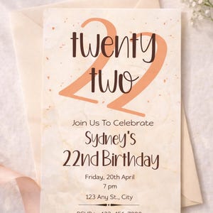Könnte beinhalten: Eine cremefarbene Geburtstagseinladung mit den Worten "twenty two" in großen orangefarbenen Buchstaben. Die Einladung ist für Sydneys 22. Geburtstag mit Datum, Uhrzeit und Ortsangaben.