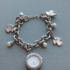 May include: Silver-toned charm bracelet featuring a watch with a white face and crystal accents. The bracelet includes angel charms, faux pearls, and a butterfly charm. The word "hope" is visible on one of the charms.