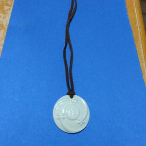 May include: A light blue ceramic pendant necklace with a floral design. The pendant is round and has a brown suede cord.