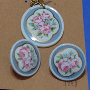 May include: A vintage Avon necklace and earrings set with a gold chain and blue and white porcelain pendants featuring a floral design. The pendants have a gold trim and a white background with pink and blue flowers.