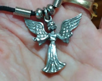 May include: Silver angel pendant necklace with a black cord. The angel has outstretched wings and a flowing gown. The necklace features silver metal accents and a clasp. The pendant is approximately 1.5 inches in height.
