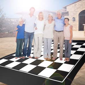 May include: A family of seven stands on a large black and white checkered game board. The board is rectangular with a white border. The people are smiling and appear to be posing for a photo.