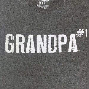 May include: Gray t-shirt with white text that reads "GRANDPA #1".
