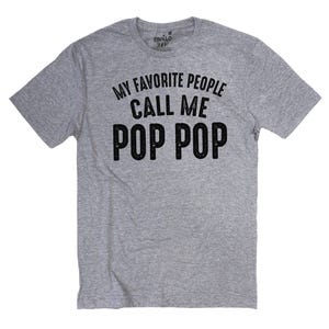 May include: A heather gray t-shirt with the text "MY FAVORITE PEOPLE CALL ME POP POP" in black. The shirt is a short-sleeved crew neck.