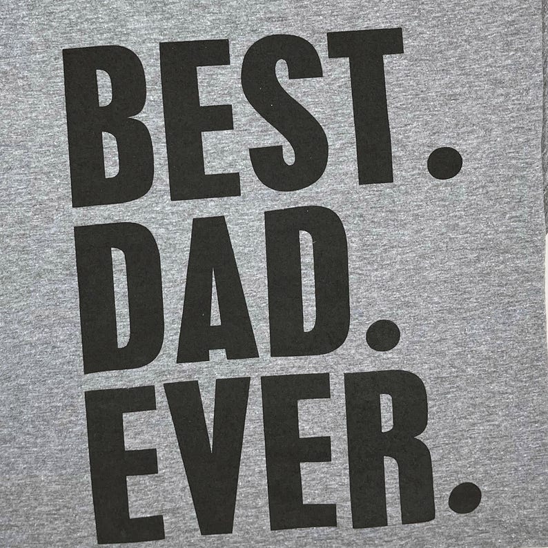 Puede incluir: Una camiseta gris con las palabras "BEST DAD EVER" impresas en letras negras grandes y audaces. El texto est&aacute; centrado y ocupa la mayor parte de la superficie de la camiseta. Dise&ntilde;o sencillo y cl&aacute;sico.