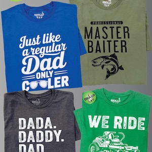 Puede incluir: Cuatro camisetas con dise&ntilde;os gr&aacute;ficos. Una camiseta azul dice "Just like a regular Dad ONLY COOLER". Una camiseta verde oliva dice "PROFESSIONAL MASTER BAITER" con un gr&aacute;fico de pez. Una camiseta gris dice "DADA. DADDY. DAD. BRUH". Una camiseta verde dice "WE RIDE AT DAWN."