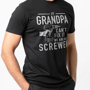Puede incluir: Camiseta negra con el texto "IF GRANDPA CAN'T FIX IT WE ARE ALL SCREWED" en gris. Tambi&eacute;n hay una ilustraci&oacute;n gris de un taladro. La camiseta es de manga corta.