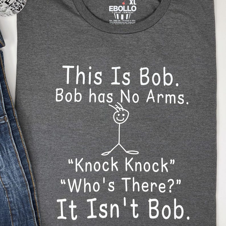Pu&ograve; includere: Maglietta grigio scuro XL con testo bianco: "This Is Bob. Bob has No Arms." Sotto, un omino stilizzato e il testo "Knock Knock" "Who's There?" "It Isn't Bob."