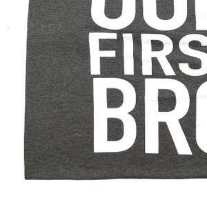 May include: A dark gray t-shirt with the text "You're my first bro" printed in white.