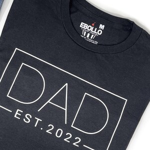 May include: Black t-shirt with a white graphic that says "DAD - EST. 2022 -" in a box.
