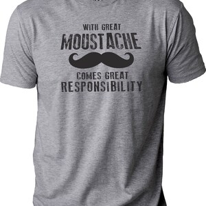 May include: A heather gray t-shirt with the text "WITH GREAT MOUSTACHE COMES GREAT RESPONSIBILITY" in black. A large black mustache graphic is centered below the word "MOUSTACHE". The shirt has a crew neck and short sleeves.