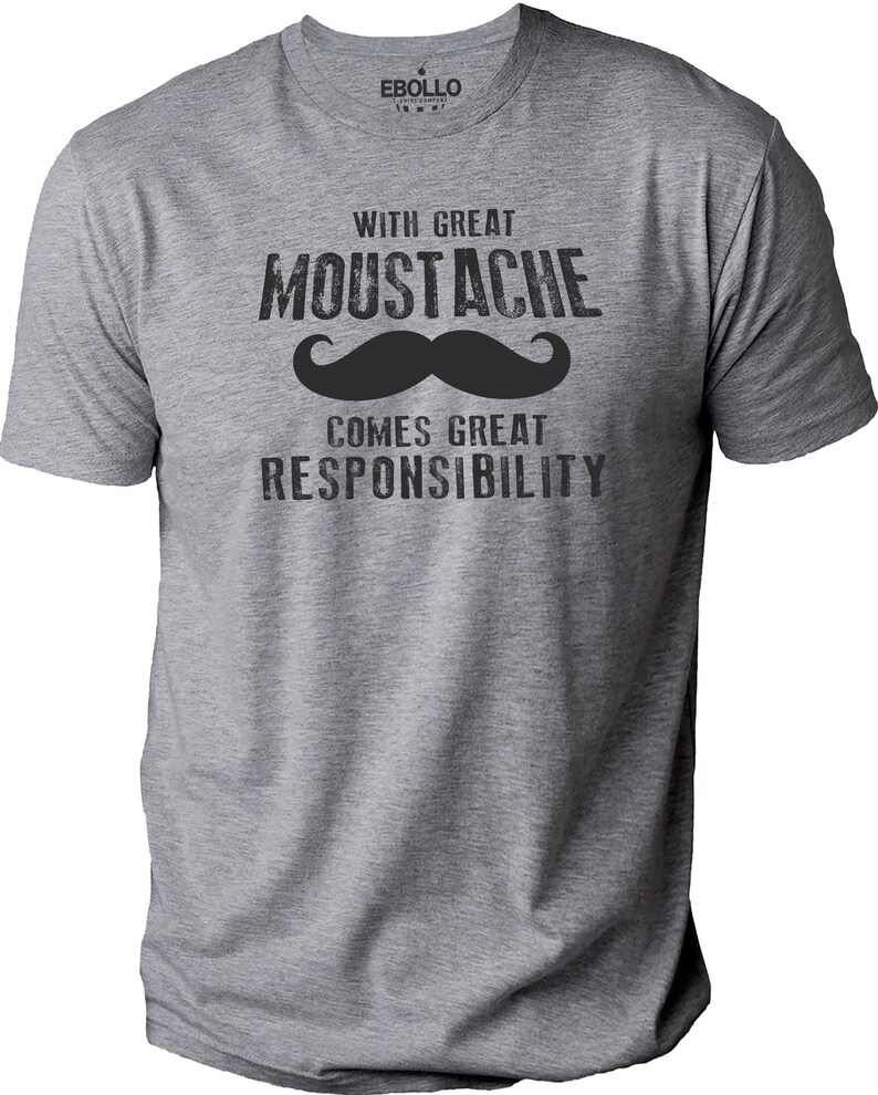 May include: A heather gray t-shirt with the text "WITH GREAT MOUSTACHE COMES GREAT RESPONSIBILITY" in black. A large black mustache graphic is centered below the word "MOUSTACHE". The shirt has a crew neck and short sleeves.