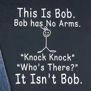 Pu&ograve; includere: T-shirt blu navy con testo bianco: "This Is Bob. Bob has No Arms." Un pupazzetto stilizzato senza braccia &egrave; disegnato sopra il testo. Sotto c'&egrave; "Knock Knock" "Who's There?" It Isn't Bob."
